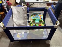 Blue Graco playpen with mesh sides and animal-themed green and colorful baby bouncer seat inside