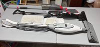 Full view of the three floor cleaning tools including the Shark steam mop with white handle, mop head with pad, Bissell MagicVac handheld vacuum, and Rubbermaid Reveal mop base without handle.