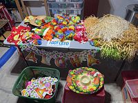 Hawaiian themed decorations and costume accessories laid out on table including colorful flower leis, grass skirts, and novelty Aloha sign.