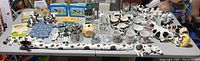 Wide view of the entire Holstein collectible lot on a white table showing mugs, teapots, creamers, tin containers, glass cups, figurines, and other assorted items.