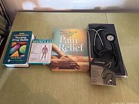 Photo showing all items lined up on a table: stethoscope in box with manual, and three books/flashcards.