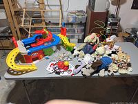 Full view of toy lot on table showing car tower, plush toys, basketball net, bead toy, and plastic cows.