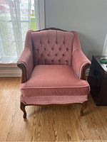 Front view of pink upholstered accent chair, showing tufted backrest and wooden carved legs.