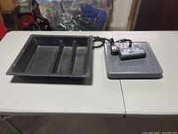 Photo of the black plastic tray with three compartments beside the postal scale platform and digital display on a white table.