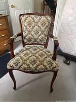 Front view of wooden Queen Anne style armchair showing padded floral upholstery and carved wooden frame.