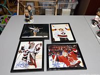 Four framed signed photos of women's hockey players and figure skaters along with two bobbleheads on a table.