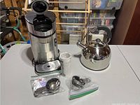 Single serve coffee maker with opened top to show brewing chamber, kettle to the right, and accessories in front.