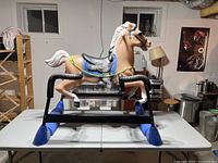 Full side view of vintage brown plastic spring rocking horse on a blue and black metal frame showing the entire horse and base.