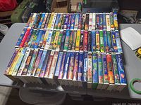 Front view of a large assortment of VHS tapes featuring kids' and Disney movies arranged in rows on a table.