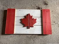 Photo of wooden Canadian flag decor showing red maple leaf center with red side panels and painted white middle boards.