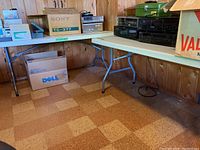 Two folding tables side by side in basement with various items on and around them. Tables have metal legs and beige tops.