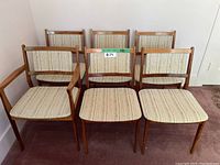 Six teak dining chairs arranged in two rows; one armchair front left, five side chairs.