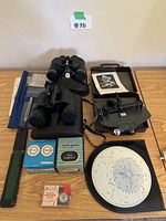 Overview of the entire lot including the binoculars, compasses, star map, tool kit and other accessories on a wooden surface.