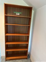 Front view of empty wooden bookshelf with six shelves and vertical wood panel back.