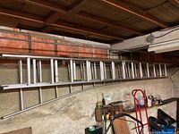 Longer aluminum extension ladder mounted horizontally on a wall with wooden shelves below.