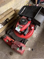 Full view of the red Troy-Bilt push mower with black grass collection bag and the smaller red fuel container in front.