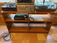 Front view of mid-century modern wooden shelf used as an entertainment piece, showing its three compartments and wood grain finish.