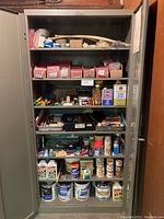 Full view of metal cabinet with shelves full of various painting supplies and hardware including paint cans and packets of screws.
