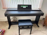 Full view of digital piano on stand with bench in front