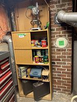 Shelf unit with three shelf compartments showing drill press on top shelf, sander in blue case, and two black cases below.