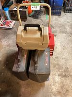Closed beige plastic toolbox on dolly, with two brown hard cases and red toolbox visible underneath