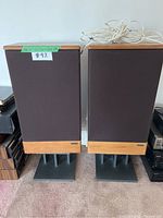 Front view of two Kenwood speakers with wooden accents and black fabric covers, placed on black stands