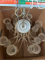 Top-down view of a glass chandelier with eight arms, glass bead chains, and candle-shaped holders, showing dust and tarnish.
