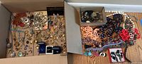 Box with organized jewelry including rings, earrings, necklaces, and loose beads displayed in two cardboard boxes.