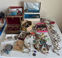 Wide photo showing entire assortment of jewelry including necklaces, bangles, earrings, brooches, and multiple jewelry boxes on table.