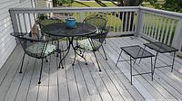 Outdoor patio set with round table and four chairs on a deck with a potted plant on the table.