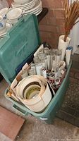 Green plastic bin filled with rolled posters and prints, some wrapped in plastic, next to wall and dishes.