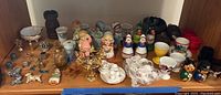 Wide shot showing assorted miniature collectibles including china tea sets, ceramic figurines, egg cups, brass candelabra, and small items.