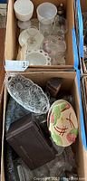 View from above showing a box with various glassware including clear and milk glass pieces, bowls, glasses, and decorative lids.