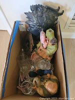 Boxed lot showing multiple items including clay figurines, glassware, metal bust, and frame