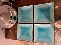 Four blue square plates arranged in a 2x2 grid, showing their front side with blue glaze and subtle gradient.