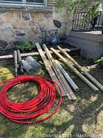 Overview of all items: pressure-treated wood, red pet pipe coil, chicken wire rolls, vapor barrier plastic, and black screening fabric laid out in a sunny outdoor space.