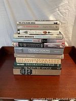 Books piled in two stacks including cooking, DIY, novels, and travel titles