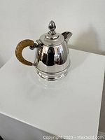 Silver-plated teapot with rattan wrapped handle shown from front and side angles on white surface