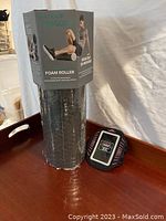 Gaiam foam roller in original packaging along with the ArmPocket phone holder on a wooden tray.
