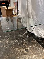 Angled side view of the square glass table top and metal frame showing the clear glass and geometric metal base design