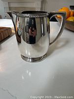 Side view of the shiny Victorian silver plated pitcher showing the handle and spout, reflective polished surface.