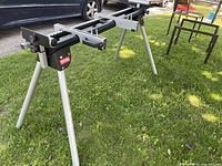 Full view of Ryobi mitre saw stand on grass, showing extendable arms and folding legs.
