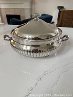 Closed view of silver plated round serving bowl with decorative finial lid and two handles