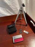 Photo showing Sony Cyber-shot camera, black Sony carrying case, two memory sticks, a white memory stick adapter, camera battery, charger and silver tripod.