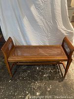 Full front view of wood and wicker bench showing weave pattern and wooden frame, arms on both ends.
