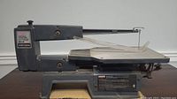 Side view of the Craftsman scroll saw showing metal arm, base, and attached blade guard with 16-inch work table.