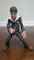 Front view of Tony Montana action figure in detailed black suit and white collar, showing facial expression and hand pose.