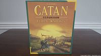 Front view of the Catan Expansion Cities & Knights box showing the detailed cover artwork with knights on horseback and setting sun.