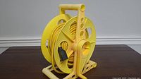 Front angled view of yellow extension cord on reel sitting on a wooden surface.