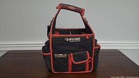 Front view of the Husky tool bag displaying multiple exterior pockets and padded handle with orange trim.